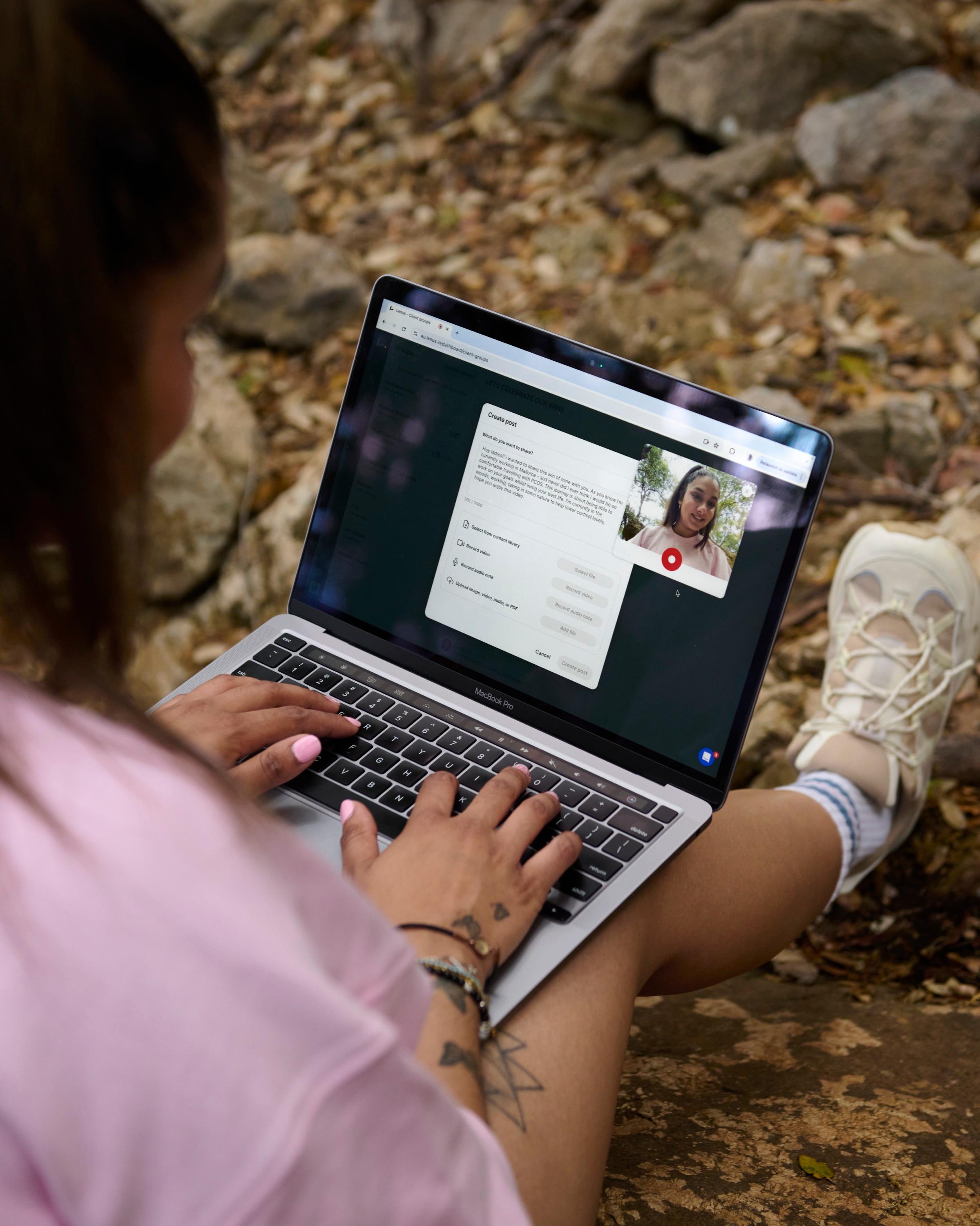A coach working on her laptop outdoors, creating a post for her clients